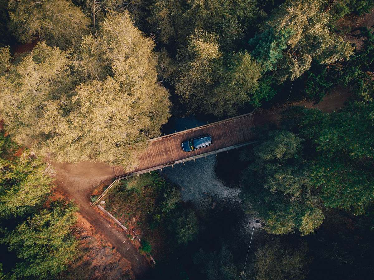 bridge aerial photo of blue car crossing bridge forest